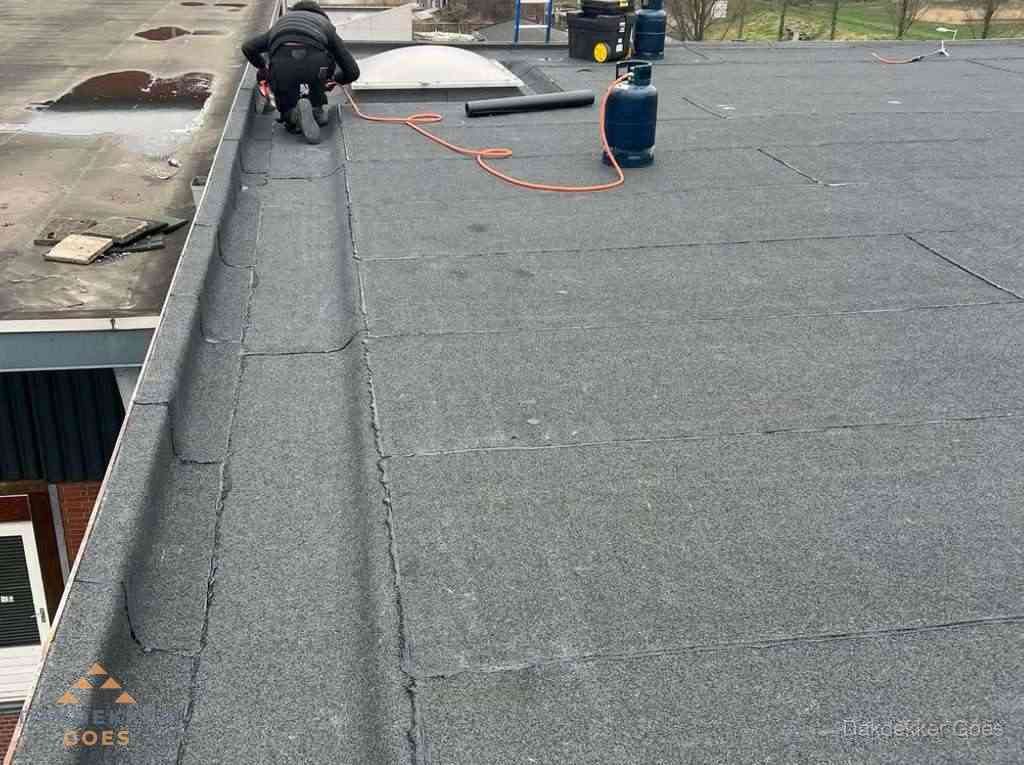 Dakdekker repareert bitumen dakbedekking op groot plat dak in Goes